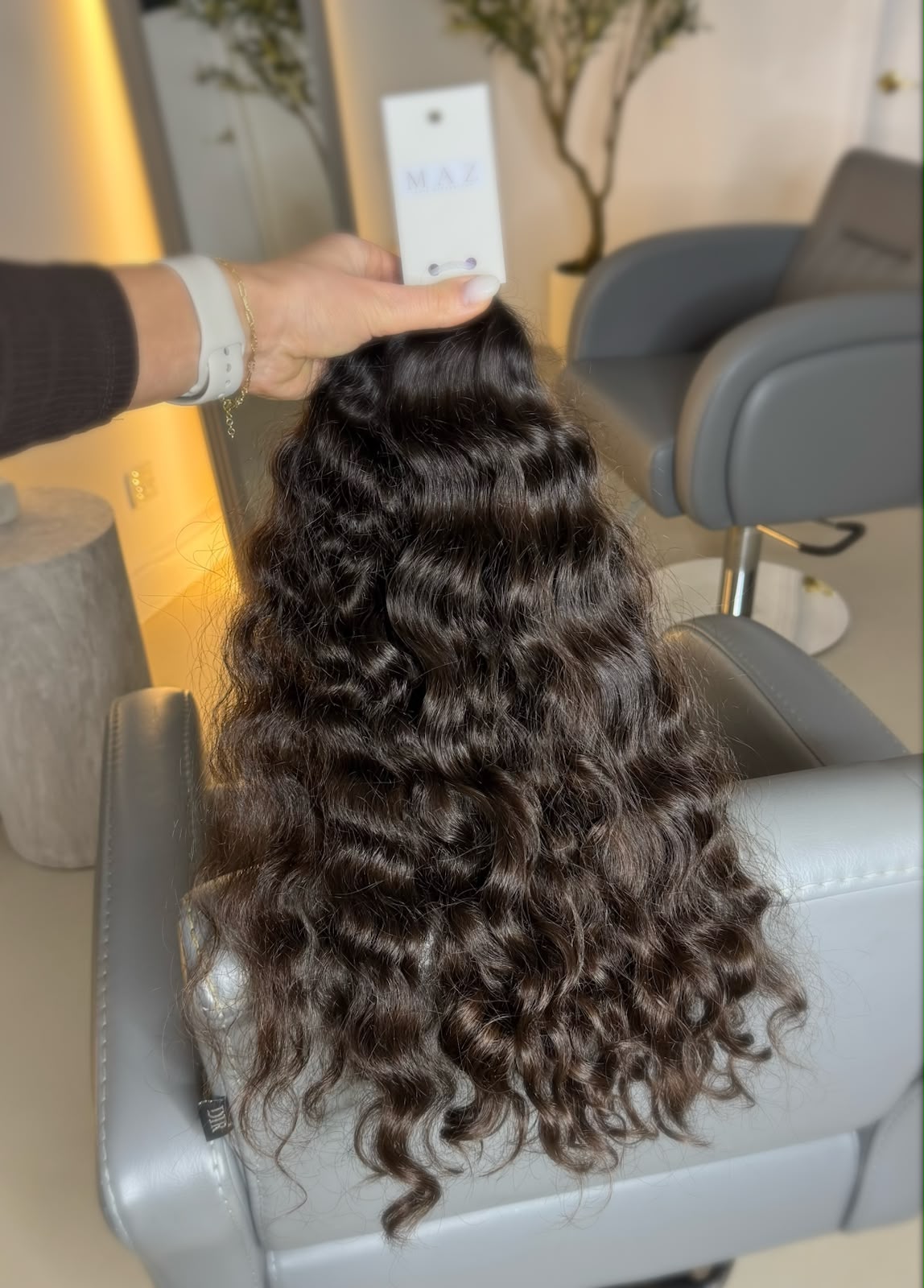 A curly hair bundle from the library, tagged with a MAZ label, laid on a pale surface