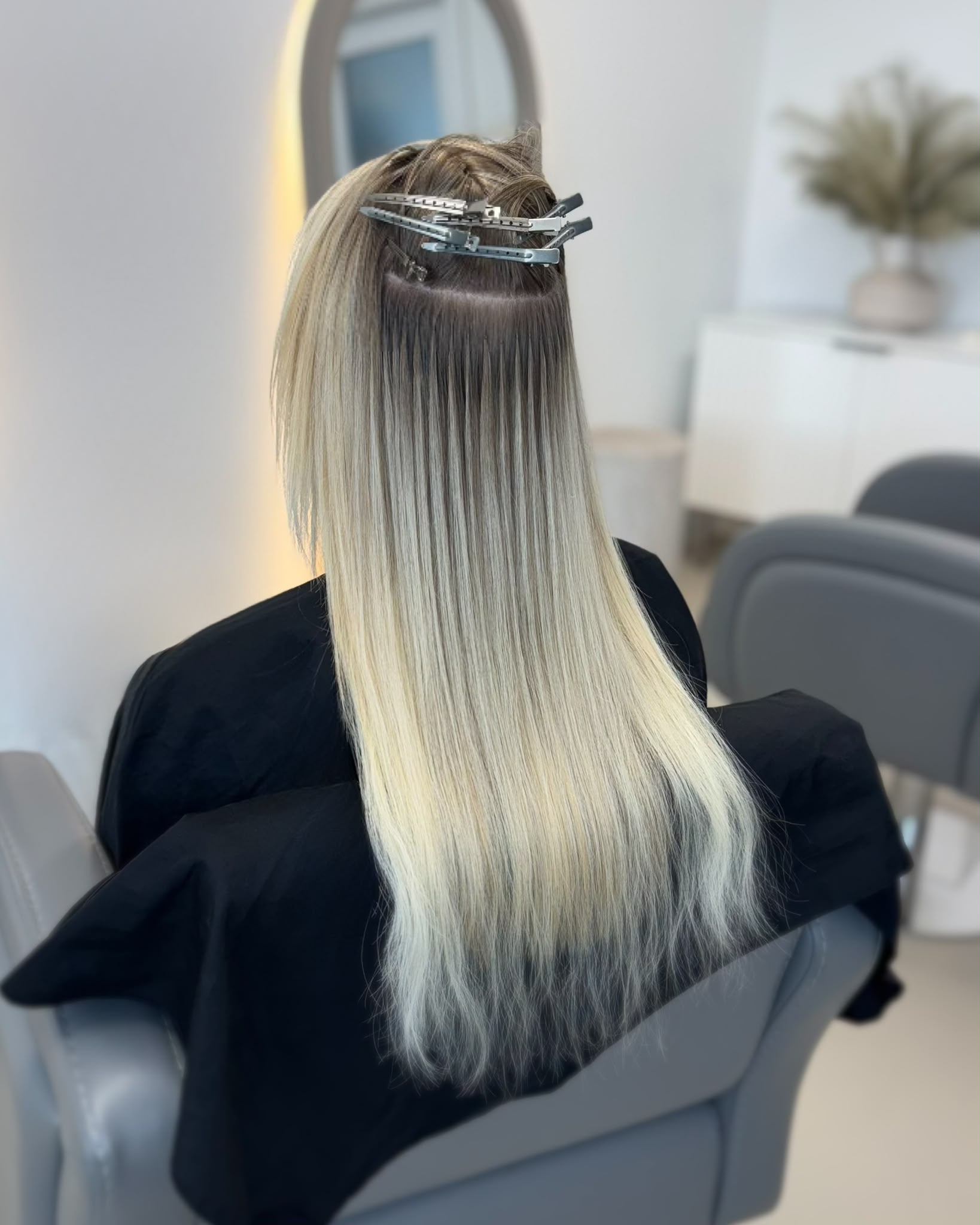 A fitting in progress: hair clipped into clean horizontal sections with a row of newly placed keratin bonds along the parting