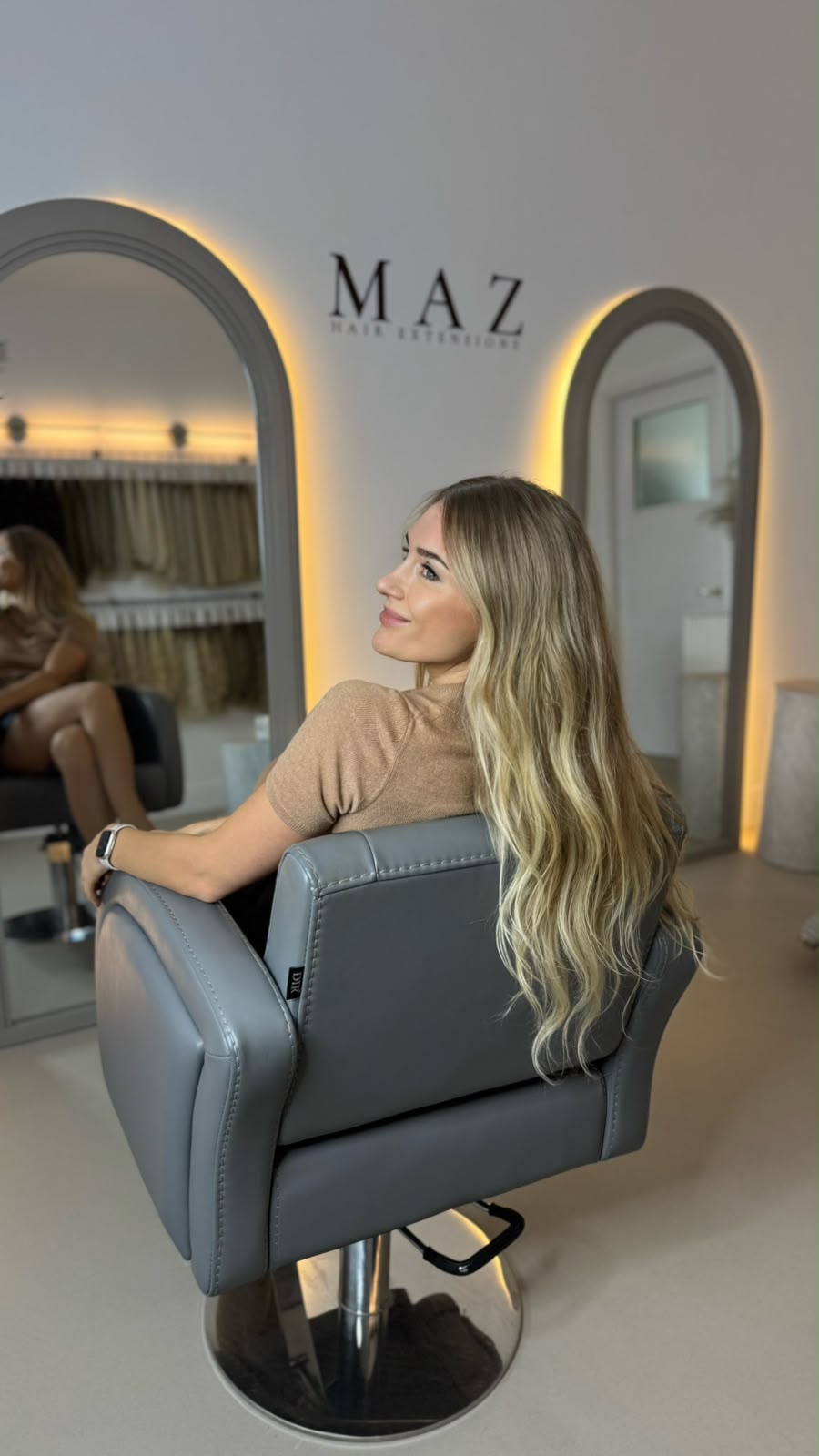 Milda seated in profile beneath the MAZ Hair Extensions wordmark on the studio wall