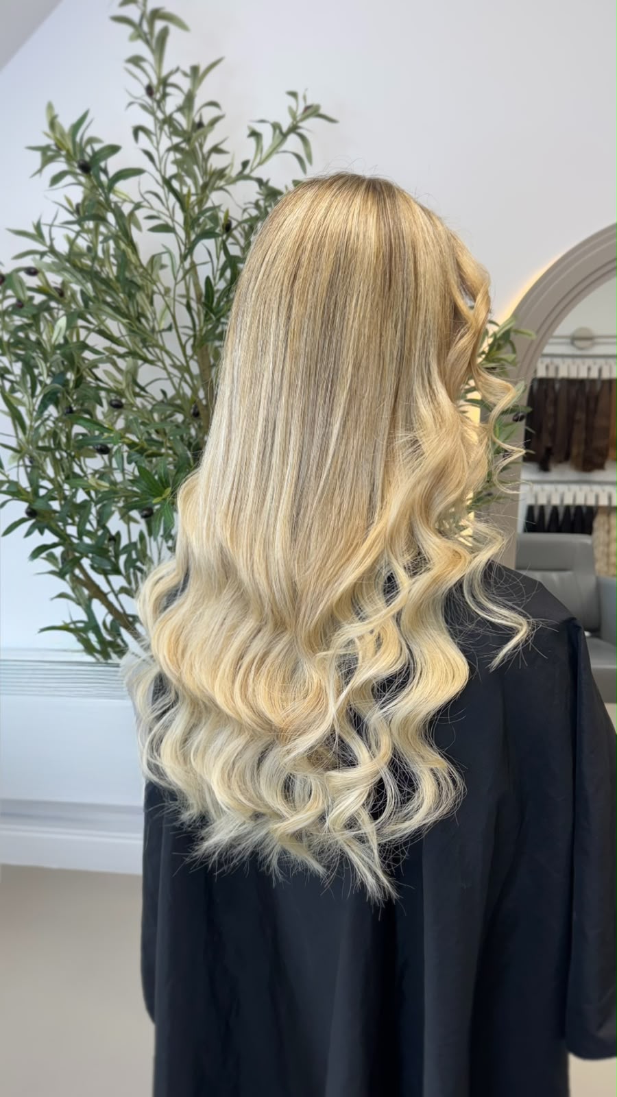 Back view of long blonde extensions finished in a soft wave, photographed against a pale studio wall